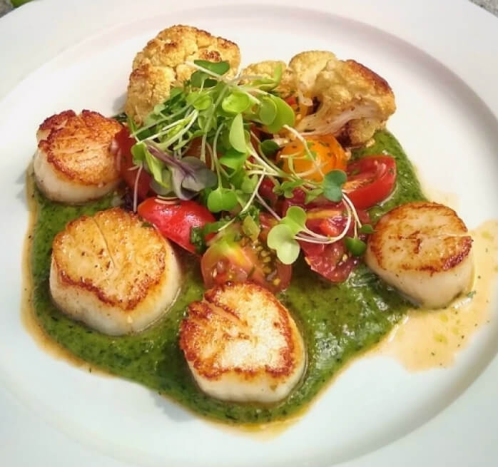 Scallops with tomatoes, green sauce, and a fresh green garnish