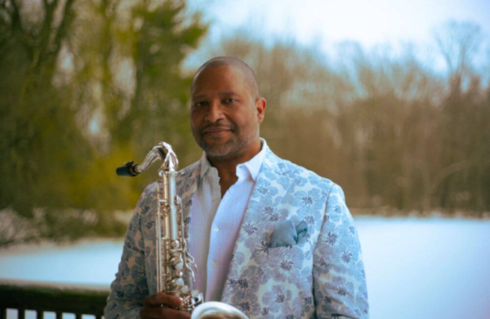 Jimmy Greene in a white and grey floral suit holding a saxophone