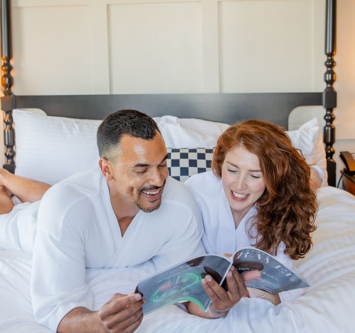 two people sitting in bed looking at magazine