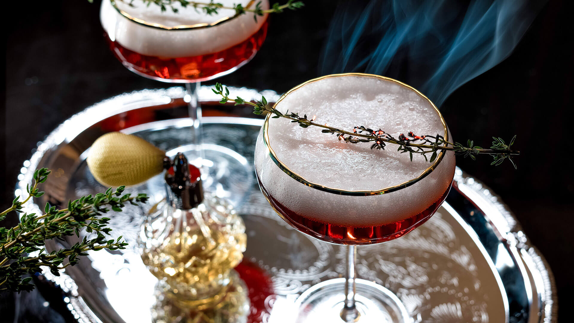 Cocktails with egg foam and fresh herb garnish on a silver platter