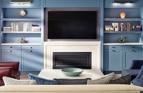 A cozy living room with a large tv above a white fireplace, flanked by blue built-in shelves and surrounded by various seating options.