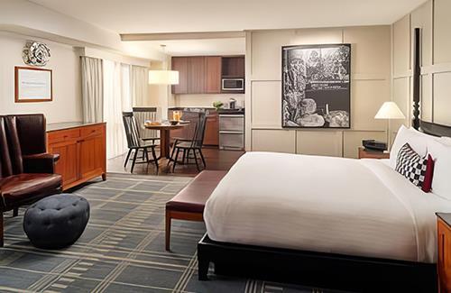 A eggshell-white hotel room with a small kitchen area and large white bed