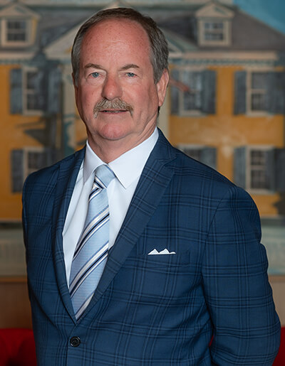 John Collins in a blue plaid suit jacket, a white dress shirt, and a diagonally striped tie
