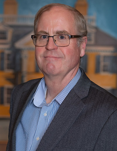 Tim Vickers in a grey suit jacket and a blue and white pinstriped dress shirt