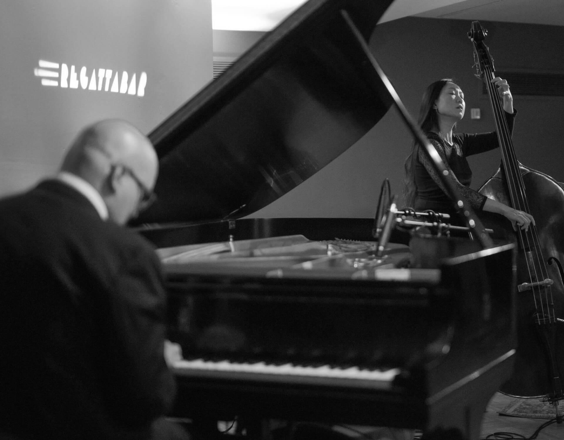 A black and white photo of people on stage playing a piano and a cello
