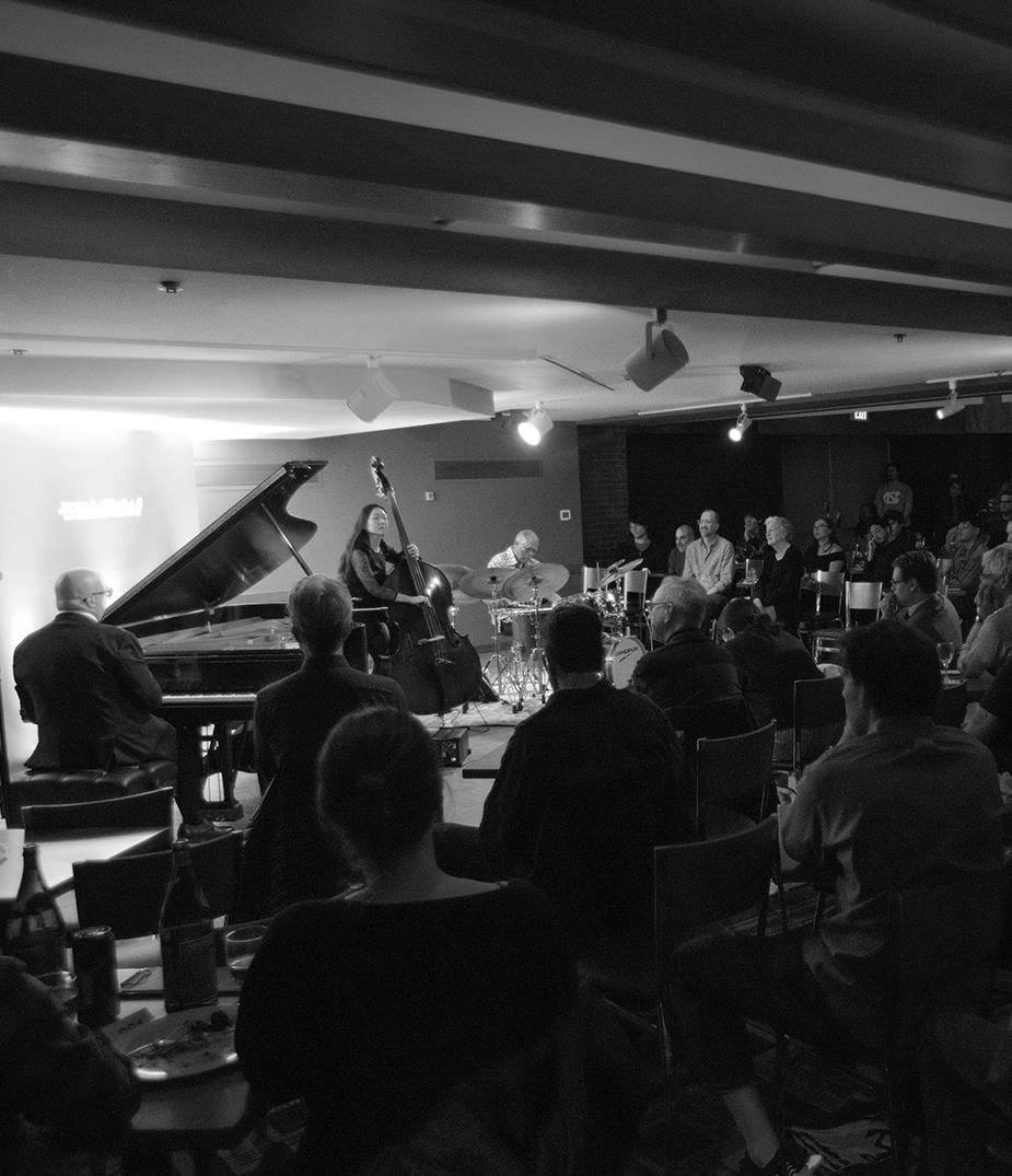 A black and white photo of people on stage playing instruments and then people in the crowd listening